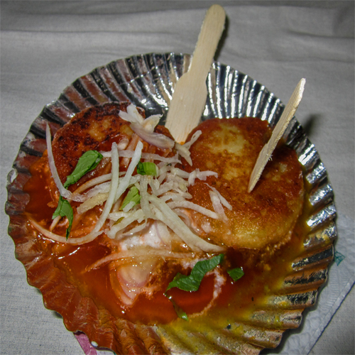 A small foil cup filled with fried potato and topped with sauces and herbs. This is a perfect example of street food.