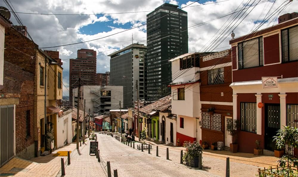 A sunny street with colourful buildings and skyscrapers in the back.