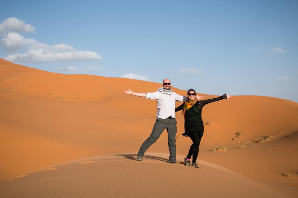 Man and woman standing in the desert as wind blows sand.