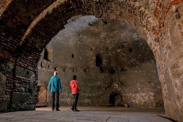 Two people in a stone room, both wearing bright coloured Prana brand hoodies.