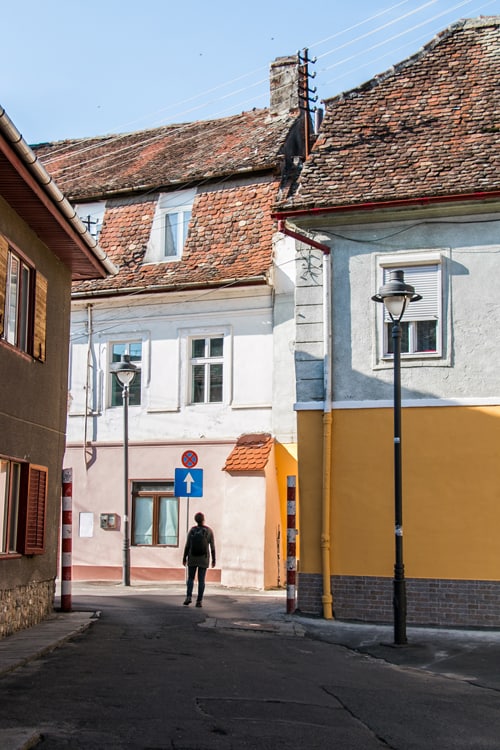 A girl walks past several yellow and pink painted buildings in a city