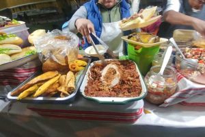 Food containers at a market with a woman using tongs to pull something out of one.