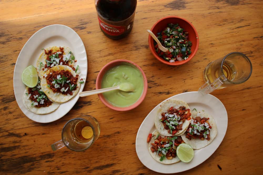 Two plates of tacos, two bowls of sauces, and some beer from a Mexican restaurant in Guatemala