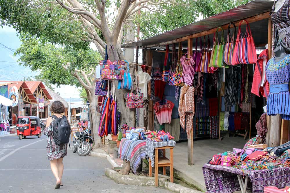 Woman walks passed a textile shop full of coloured clothing in San Juan Lake Atitlan