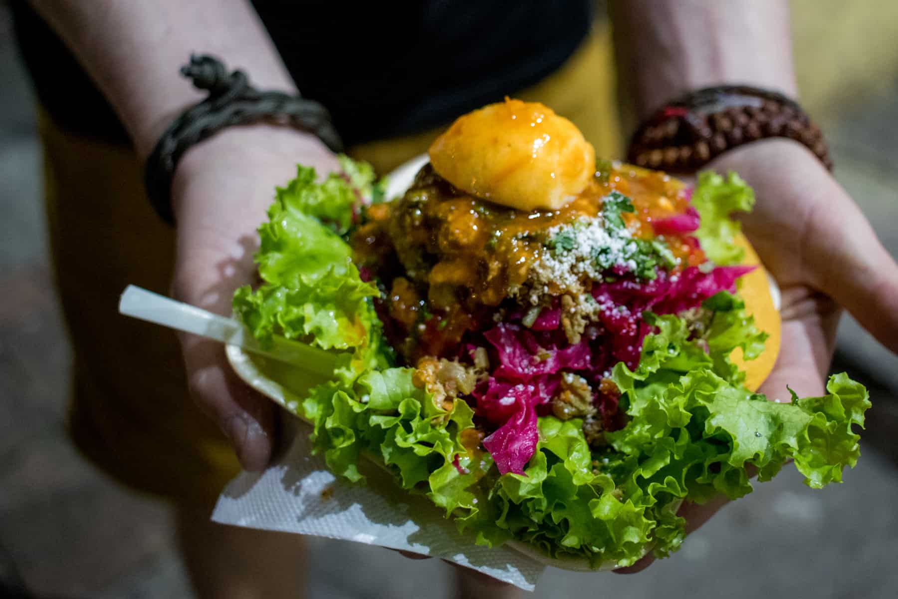 Hands holding a plate with a fried tortilla, topped with lettuce, meat, cabbage, egg and sauce in Antigua