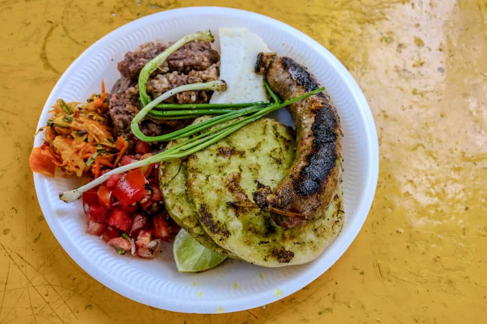 Yellow table with a white plate full of rice, beans, tomatoes and sausage