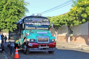 Green and red school bus on the side of the road with the words Santa Ana and Juayua in the window
