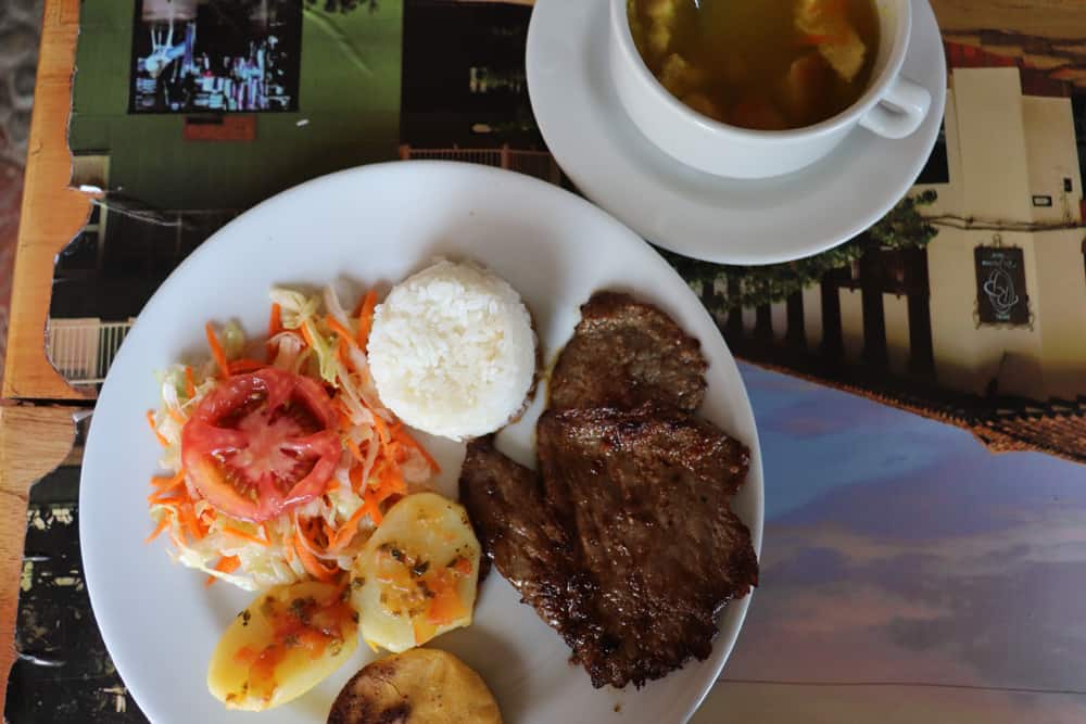 Bowl of soup and a plate with rice, potatoes, salad and beef