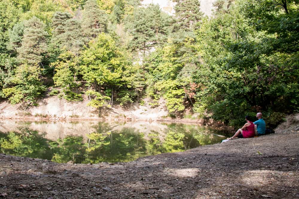 Two people sit beside a pond