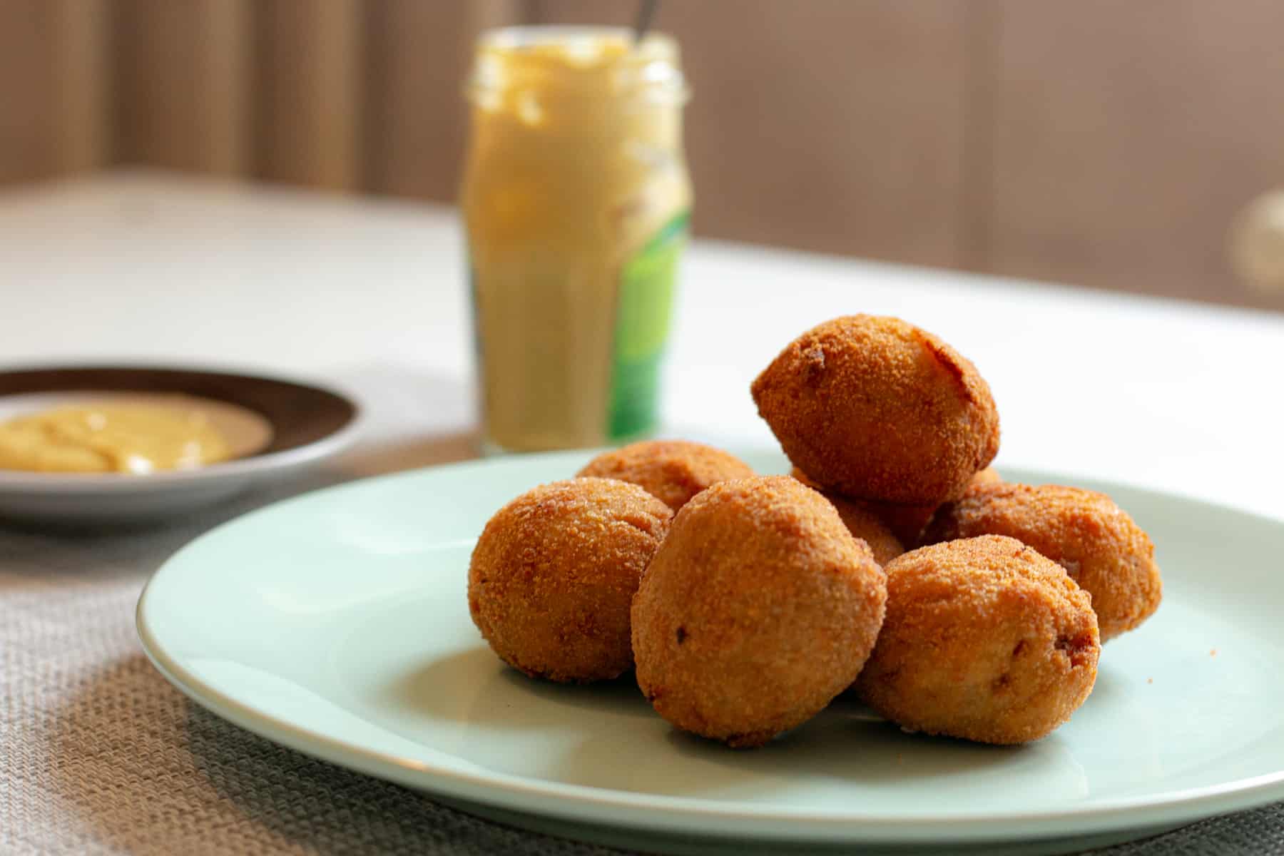 Deep fried round snacks on a plate with a jar of mustard in the background.
