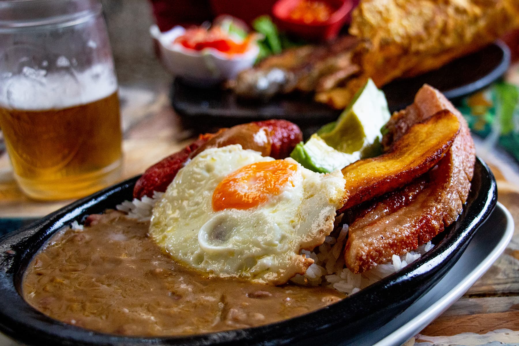 Iron skillet filled with beans, sausage, plantains, egg and avocado. Bandeja paisa is a classic Colombian dish.