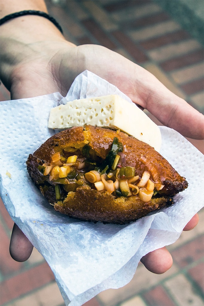 Hand holding a fried fritter in Colombia with a piece of cheese on the side.