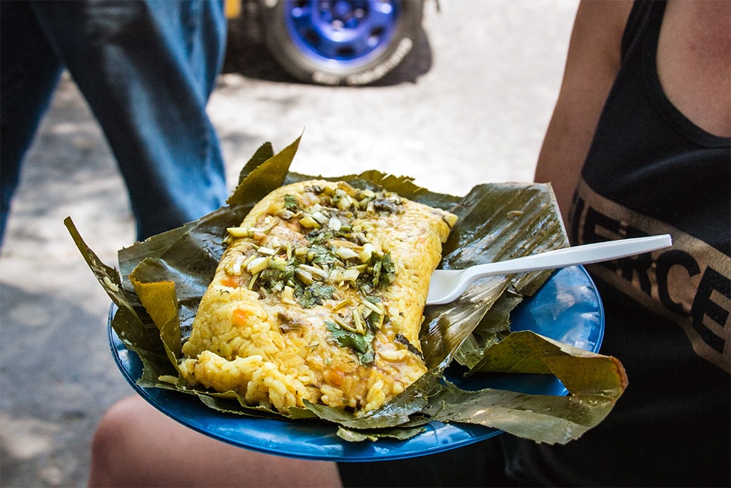 Plate with an open banana leaf stuffed with a yellow rice filled with vegetables.