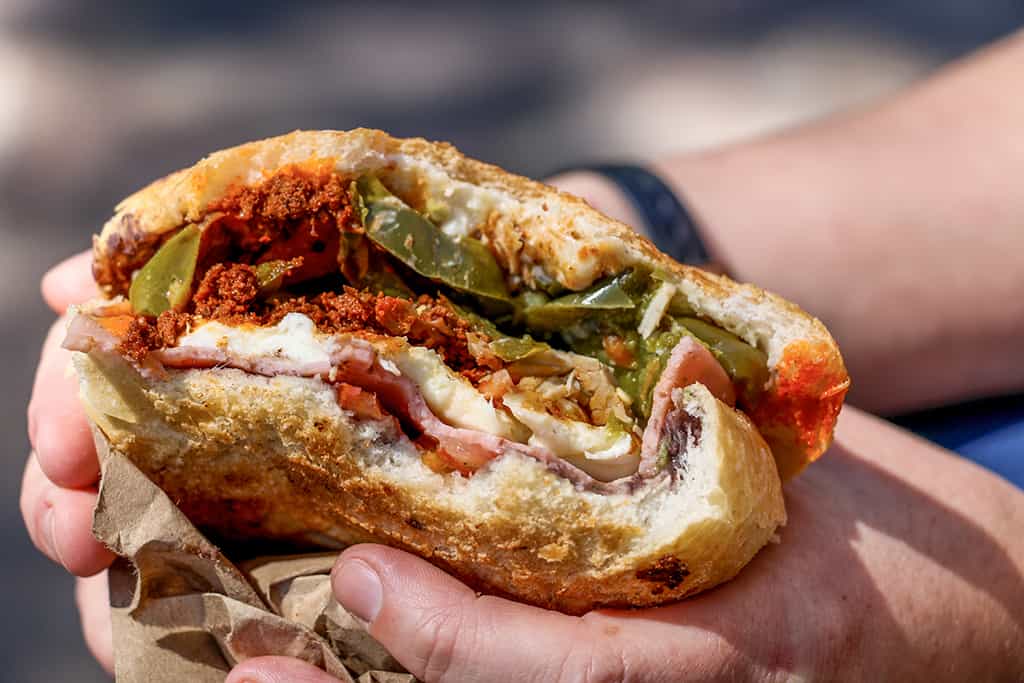 Hand holding a sandwich filled with meat, cheese and jalapenos.