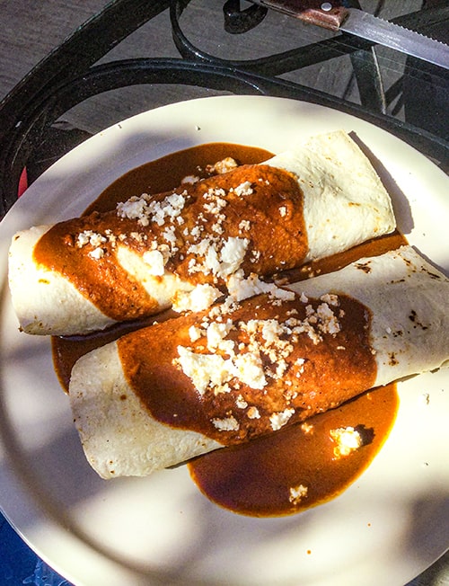 Two rolled tortillas covered in a brown sauce and crumbled white cheese.