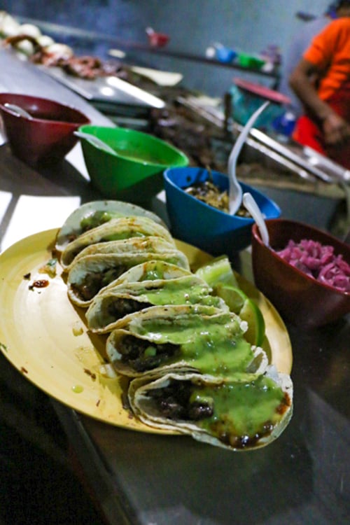 Yellow plate with tacos on it filled with meat and a creamy green sauce.