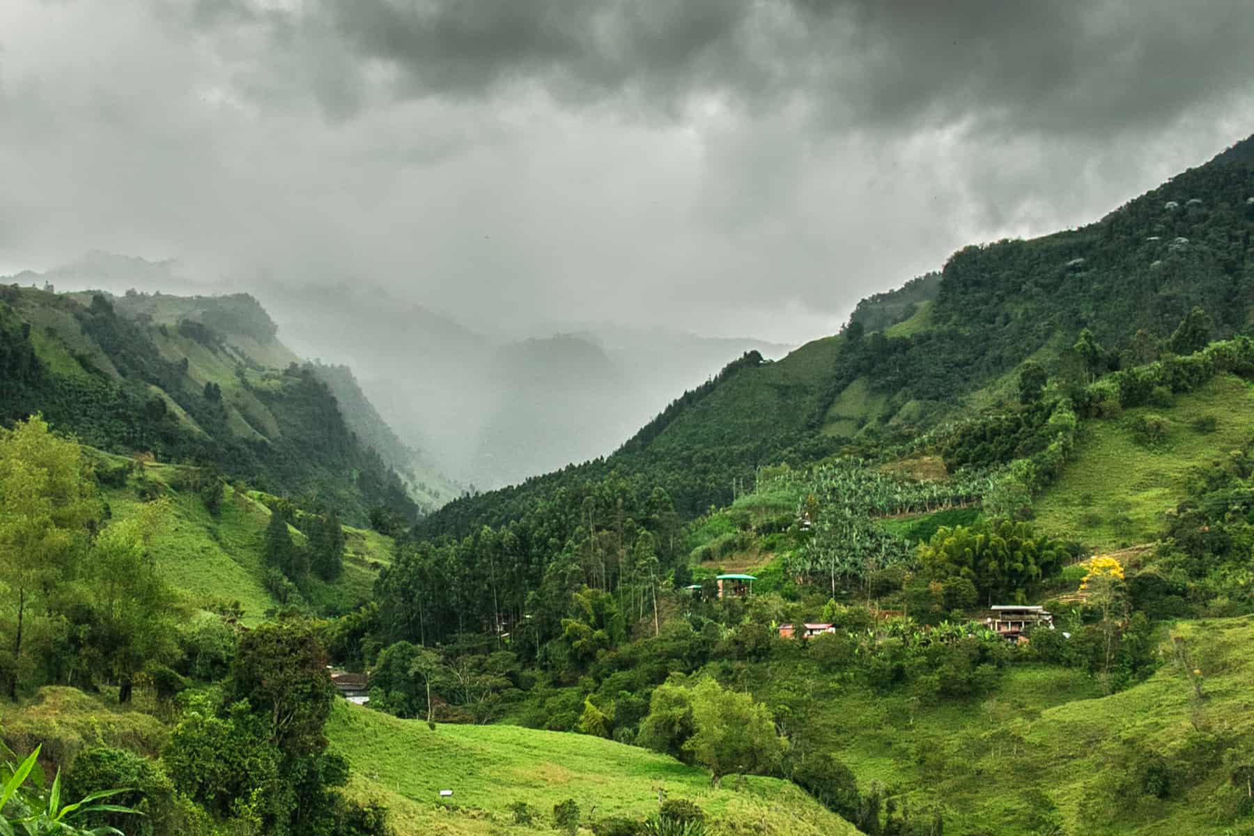 Rolling green hills in a deep valley with dark rain clouds in the sky.