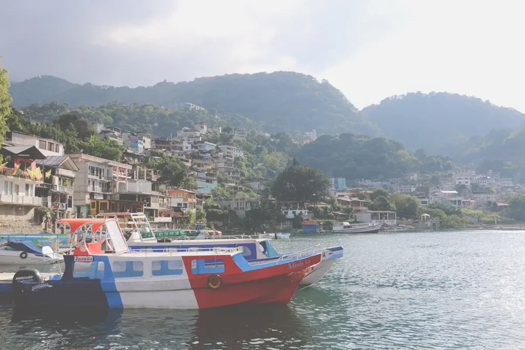 Red, white, and blue boat in the water, with a colourful village of San Pedro in the background.