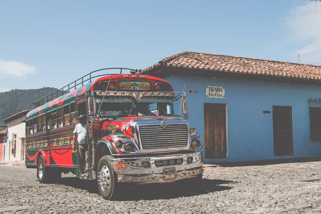 Red school bus with chrome and colourful decals beside a blue building.