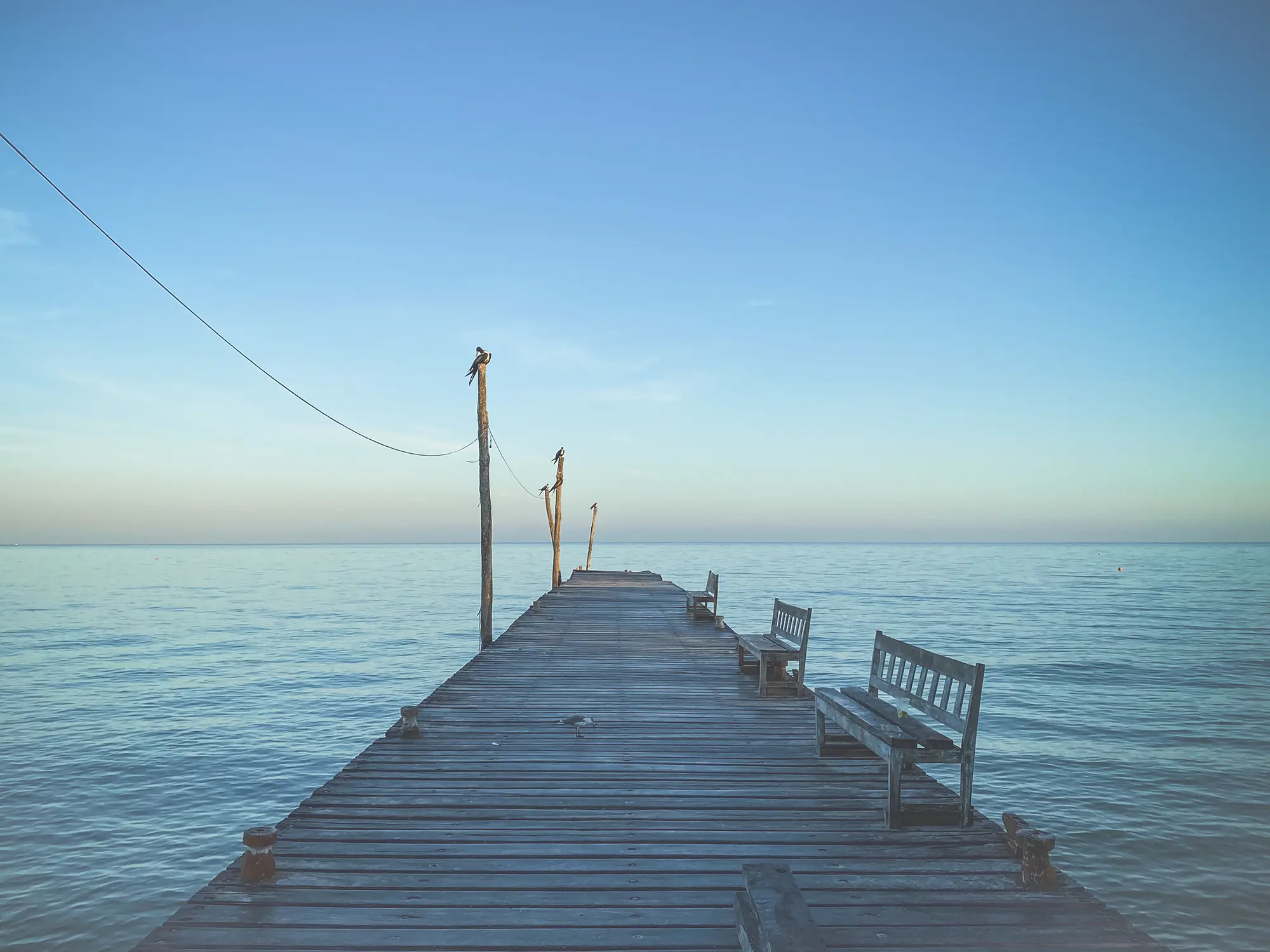 Looking out at a wooden dock stretching into a blue sea at sunrise.