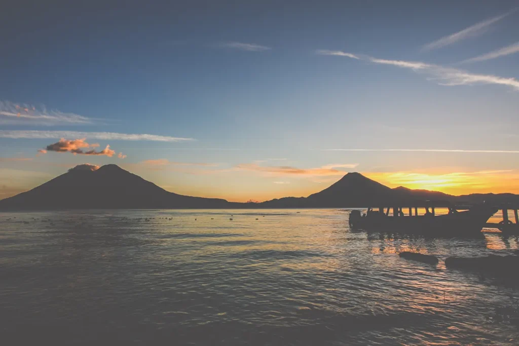 Sunset over a Lake with a boat in the foreground and two volcanoes in the back.