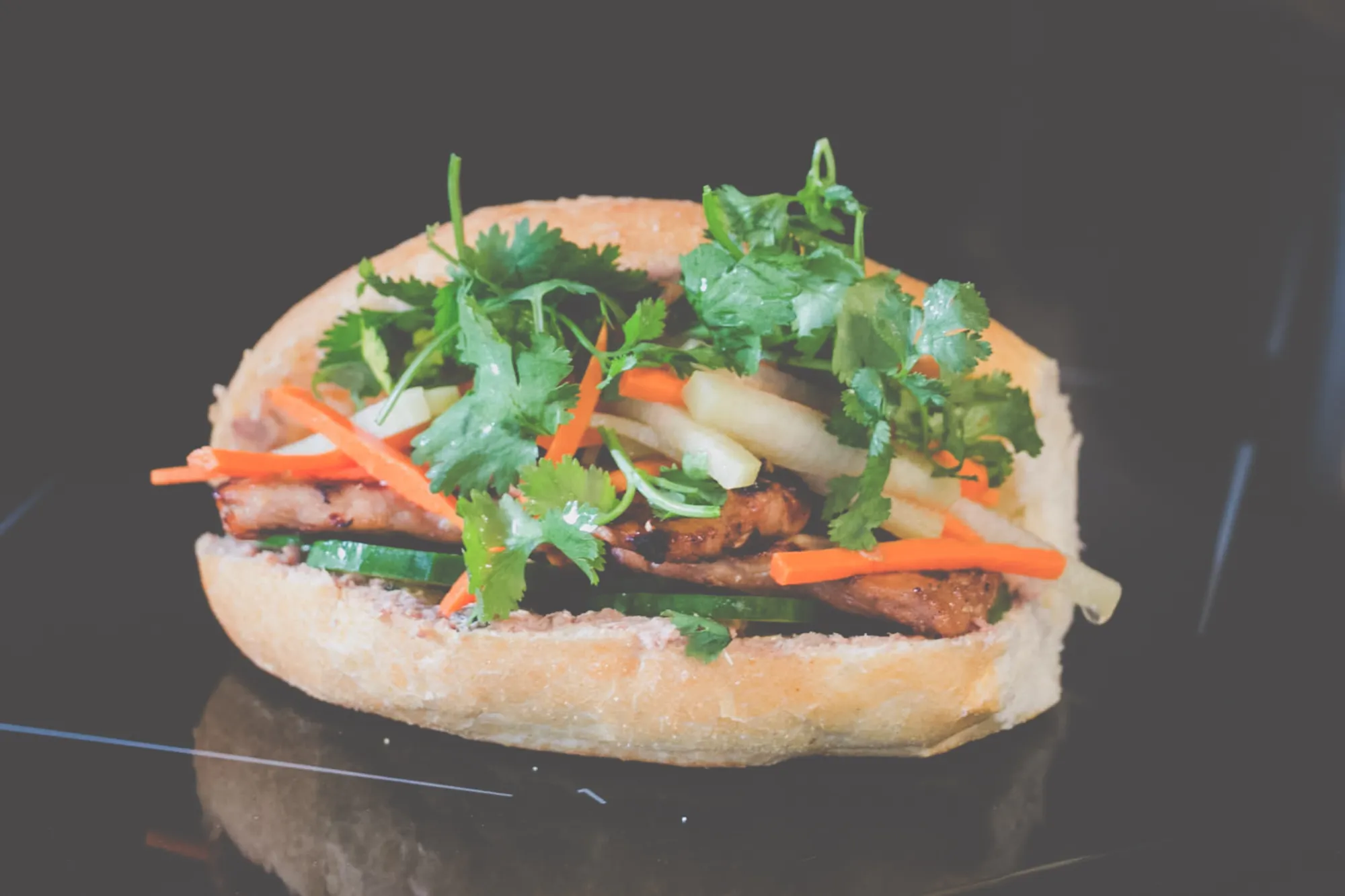 Banh Mi, a Vietnamese sandwich. A bun filled with grilled chicken, cucumber, pickled vegetables and green cilantro.
