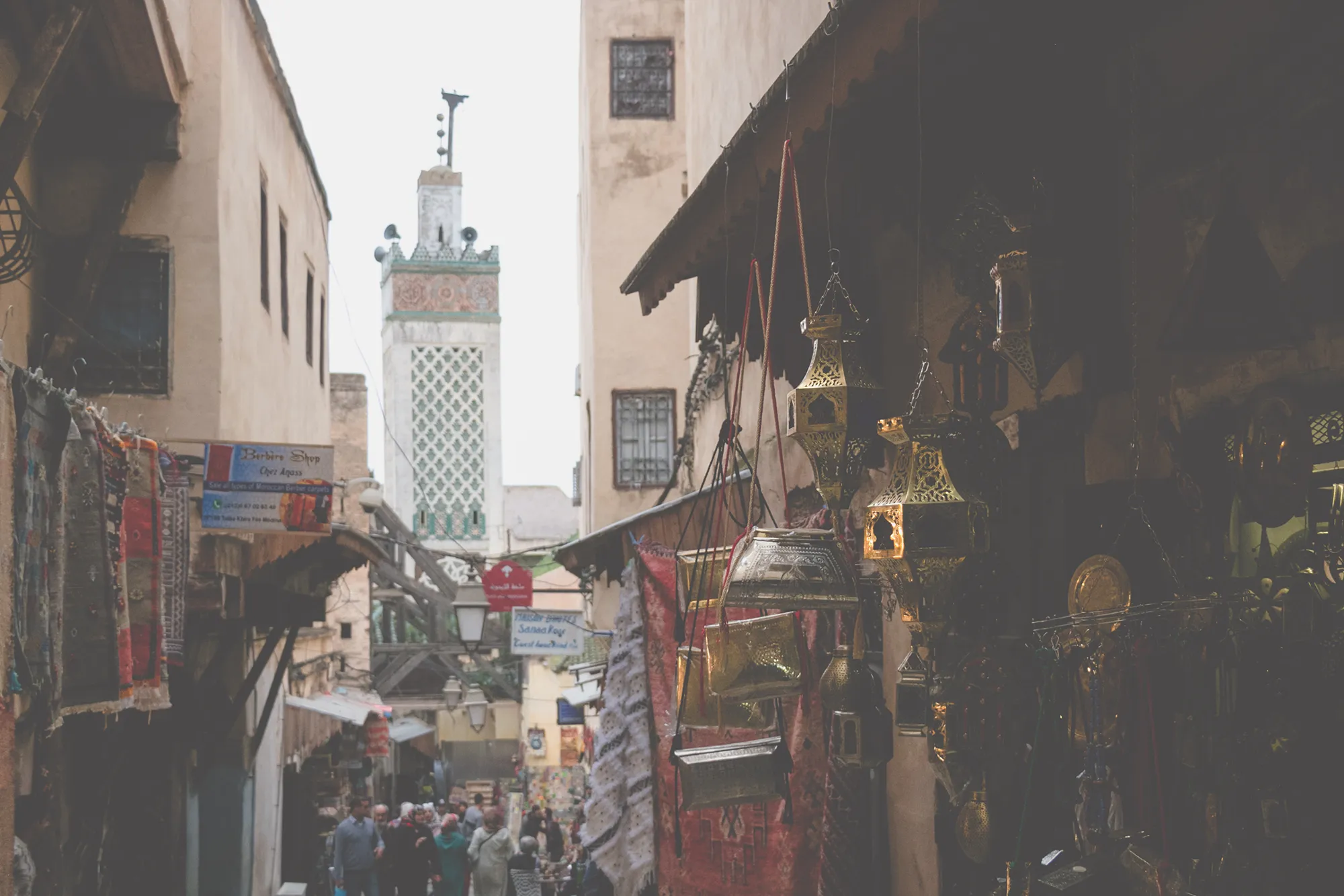 A busy street with many souvenirs in stalls along the side, with the minaret of a Mosque in the background.