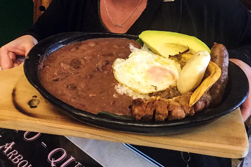 Large iron skillet filled with meat, eggs, beans and avocado.