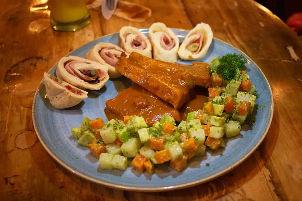 Blue plate with a salad, braised pork, and bread stuffed with oilves.