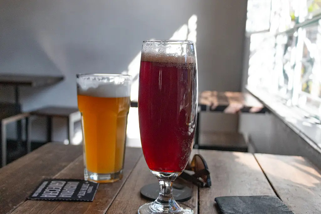 Two large glasses of beer on a wooden table. One orange, the other dark red.
